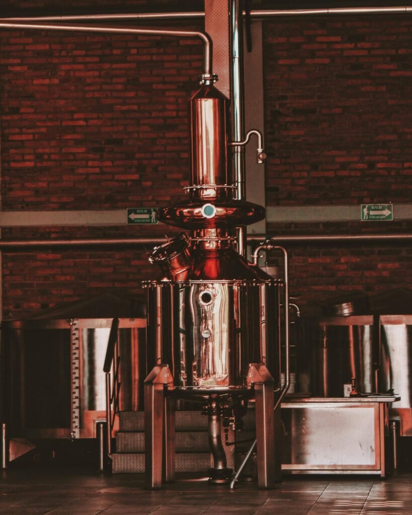 pexels-photo-8914112-8914112 Close-up of stainless steel distillery equipment in an industrial setting, featuring pipes and machinery.